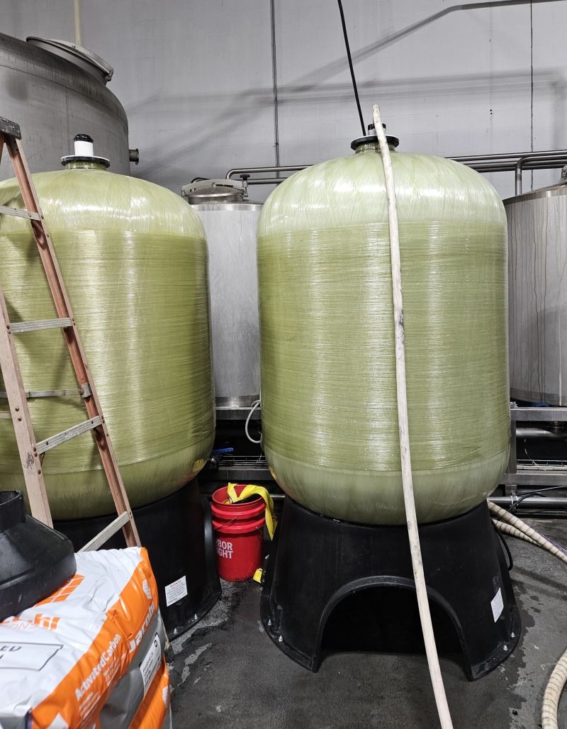 Two 48-inch carbon filtration tanks staged for media loading with activated carbon, fitted with 3900 control valves, Hoffman Soft Water industrial filtration